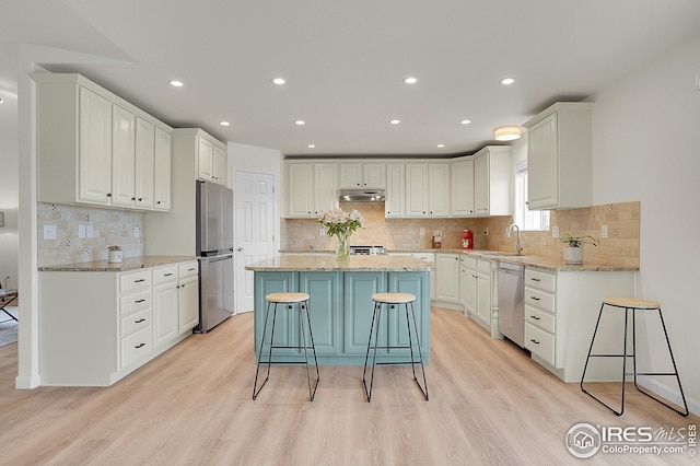kitchen featuring appliances with stainless steel finishes, a sink, under cabinet range hood, a kitchen island, and white cabinets