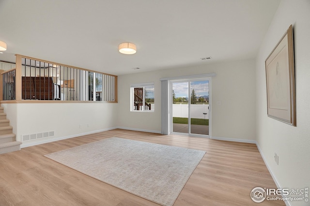 unfurnished living room featuring light wood-type flooring, baseboards, and stairway