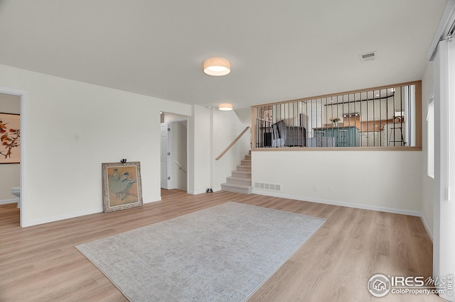 unfurnished living room with wood finished floors, stairway, and baseboards