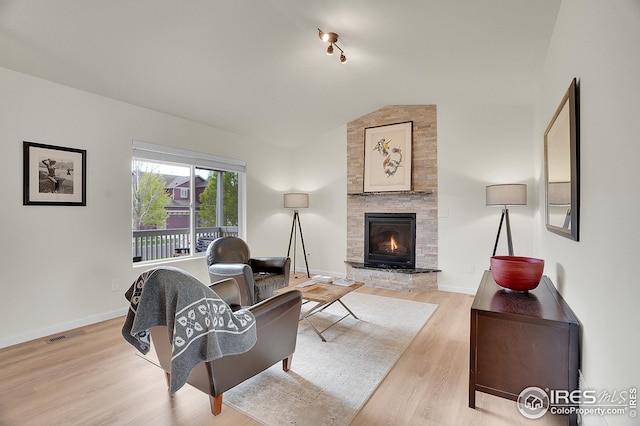 living room with vaulted ceiling, light wood-type flooring, a stone fireplace, and baseboards