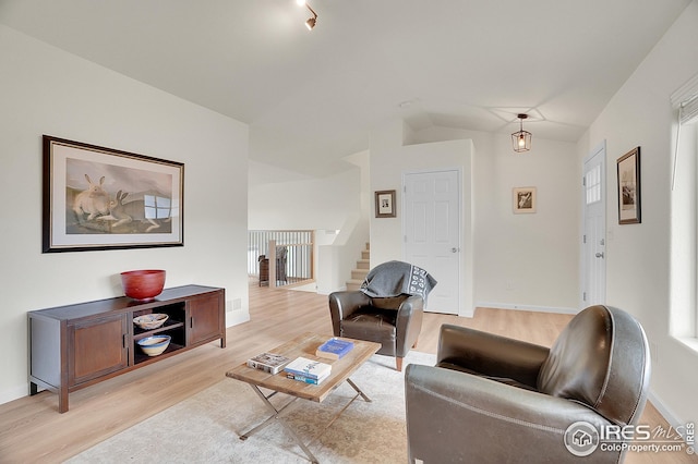 living area featuring stairs, light wood-type flooring, lofted ceiling, and baseboards