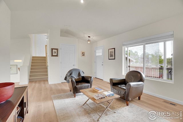 living area featuring stairs, light wood-type flooring, lofted ceiling, and baseboards