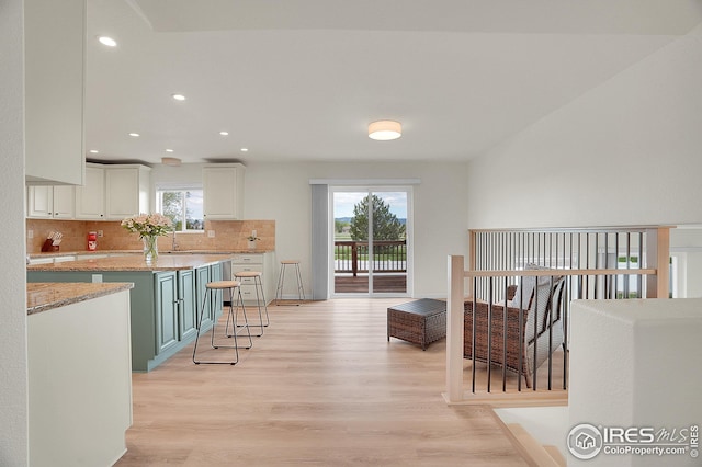 kitchen with light wood-style flooring, decorative backsplash, recessed lighting, white cabinetry, and light stone countertops