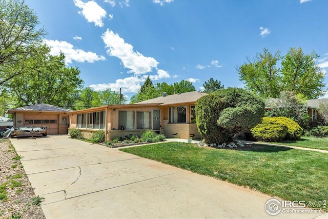 single story home with a front yard, concrete driveway, brick siding, and a garage
