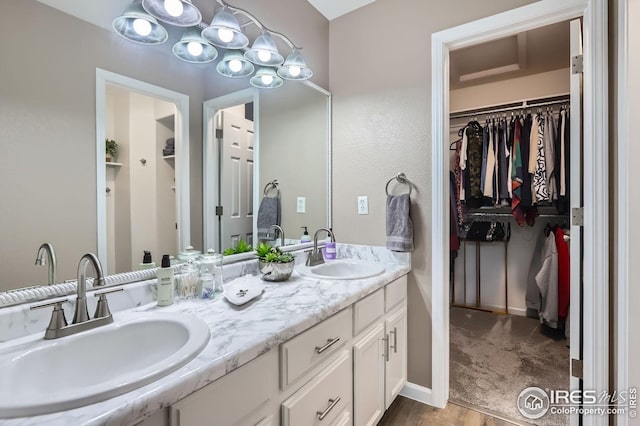 full bath with a walk in closet, double vanity, and wood finished floors