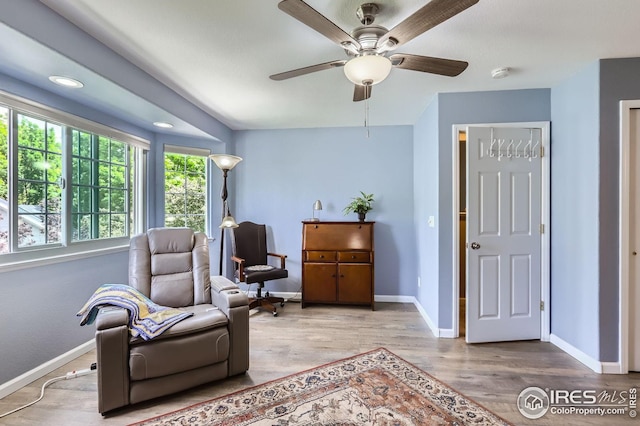 living area with baseboards, wood finished floors, and a ceiling fan