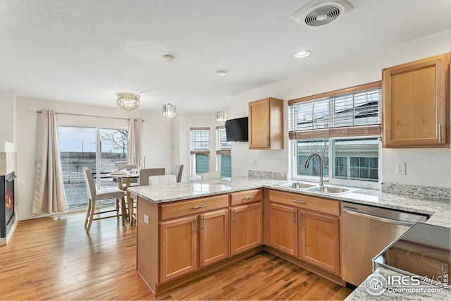 kitchen featuring a sink, dishwasher, a peninsula, light wood-style floors, and light stone counters