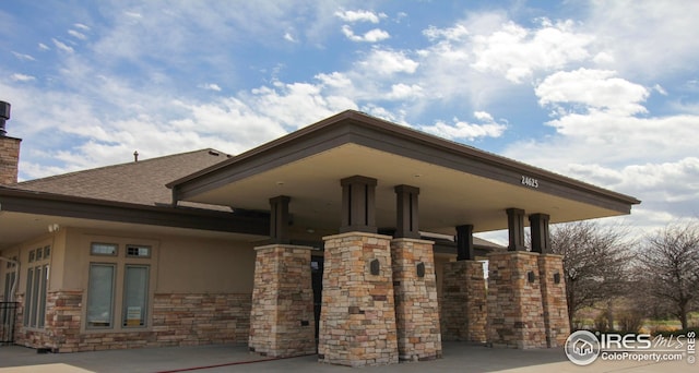 view of home's exterior with stone siding, stucco siding, a chimney, and roof with shingles