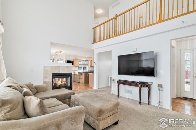 living room featuring plenty of natural light, a towering ceiling, light carpet, baseboards, and a tiled fireplace