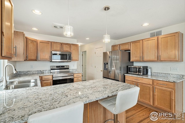 kitchen with stainless steel appliances, a sink, a peninsula, pendant lighting, and light wood-style flooring
