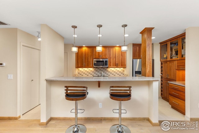 1140 Portland Pl Unit 207, Boulder, CO 80304 - kitchen featuring stainless steel appliances, a peninsula, tasteful backsplash, brown cabinetry, and a kitchen breakfast bar