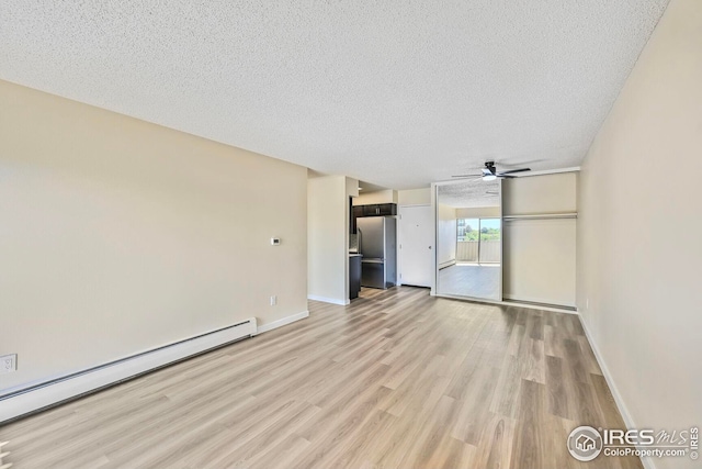 unfurnished living room with baseboard heating, light wood-type flooring, a textured ceiling, ceiling fan, and baseboards