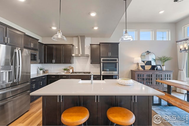 6752 Castello St, Timnath, CO 80547 - kitchen with stainless steel appliances, wall chimney exhaust hood, a sink, light wood finished floors, and a kitchen bar