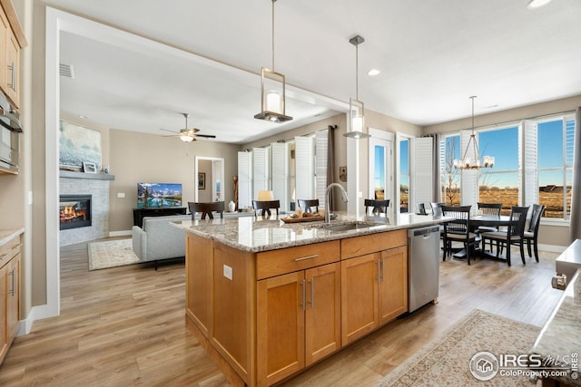 1030 Larimer Ridge Pkwy, Timnath, CO 80547 - kitchen with a sink, stainless steel dishwasher, a glass covered fireplace, light wood finished floors, and a kitchen island with sink