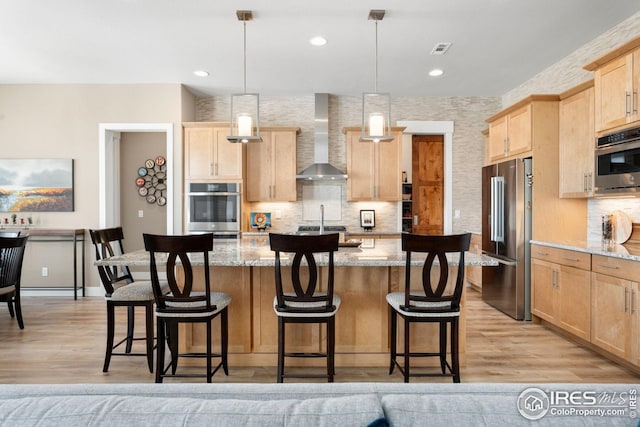 1030 Larimer Ridge Pkwy, Timnath, CO 80547 - kitchen with stainless steel appliances, light brown cabinets, wall chimney range hood, light wood-style flooring, and recessed lighting