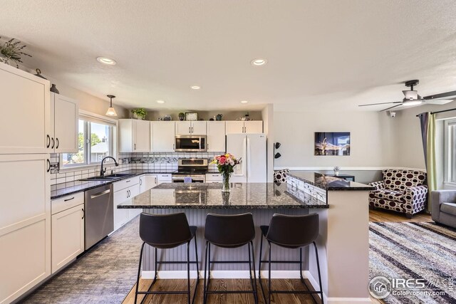 2447 E 100th Way, Thornton, CO 80229 - kitchen with appliances with stainless steel finishes, a sink, a kitchen island, backsplash, and white cabinetry
