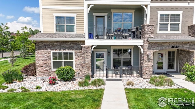 4642 Hahns Peak Dr Unit 101, Loveland, CO 80538 - view of front of home with a balcony, stone siding, a front yard, and a shingled roof