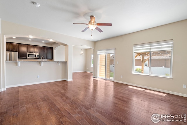 848 Shirttail Peak Dr, Windsor, CO 80550 - unfurnished living room featuring arched walkways, a ceiling fan, dark wood-type flooring, and baseboards