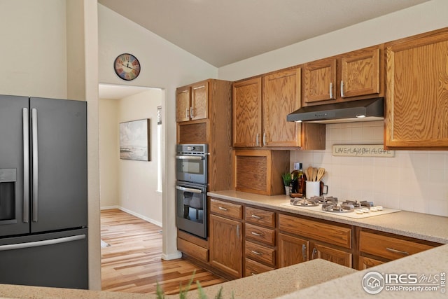 1427 Reeves Dr, Fort Collins, CO 80526 - kitchen featuring stainless steel appliances, under cabinet range hood, brown cabinets, decorative backsplash, and lofted ceiling