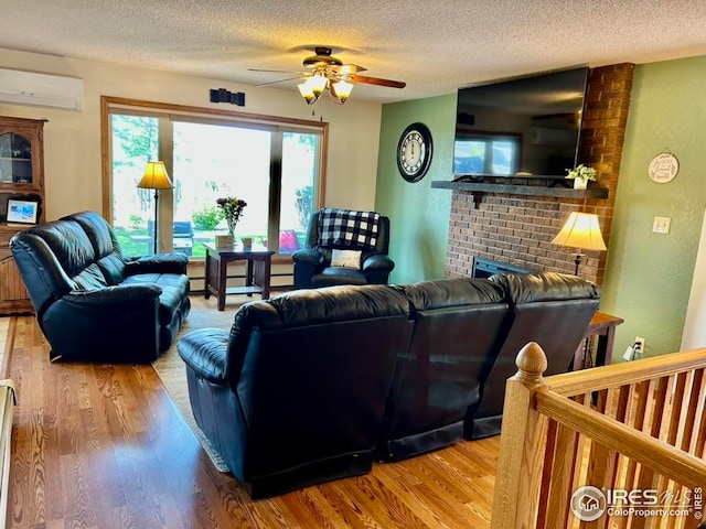 1722 Pheasant Rdg, Sterling, CO 80751 - living room featuring a wall mounted AC, wood finished floors, a textured ceiling, a ceiling fan, and a brick fireplace