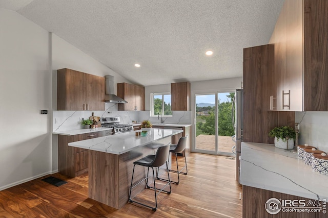 2037 Spencer St, Longmont, CO 80501 - kitchen featuring wall chimney exhaust hood, appliances with stainless steel finishes, a textured ceiling, lofted ceiling, and a center island