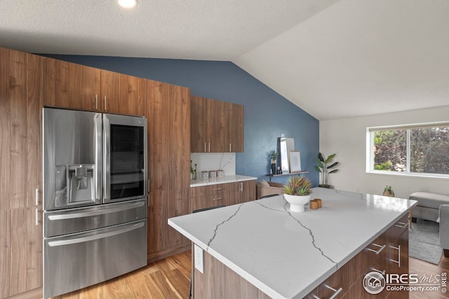 2037 Spencer St, Longmont, CO 80501 - kitchen featuring stainless steel refrigerator with ice dispenser, vaulted ceiling, light wood-style floors, brown cabinets, and light stone countertops
