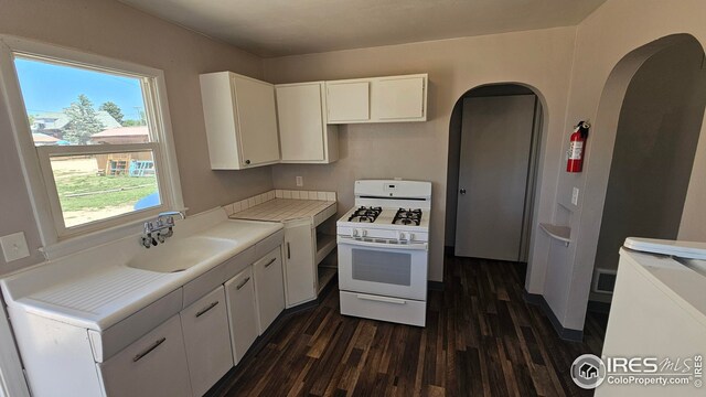 351 E 2nd St, Akron, CO 80720 - kitchen featuring white gas range, dark wood-style flooring, arched walkways, and white cabinets
