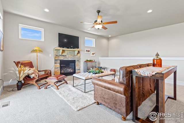 living room featuring ceiling fan, light carpet, and a stone fireplace