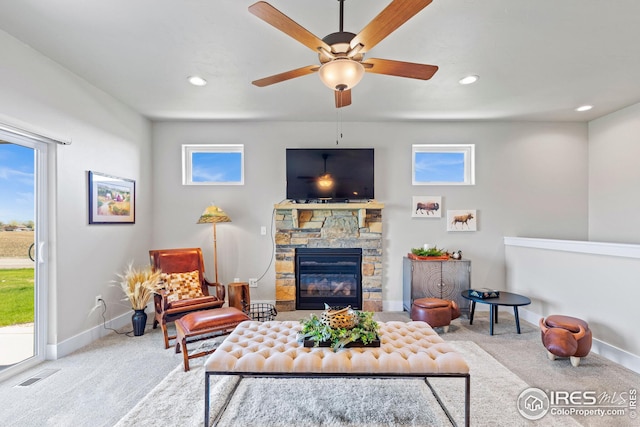 carpeted living room with ceiling fan, a wealth of natural light, and a stone fireplace