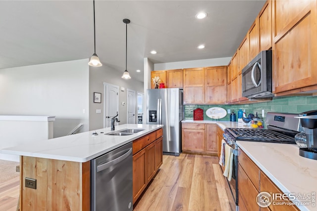 kitchen featuring appliances with stainless steel finishes, light wood-type flooring, tasteful backsplash, and a center island with sink