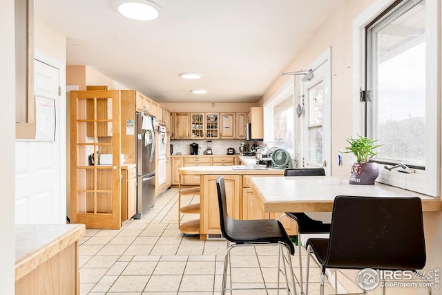 kitchen featuring light tile floors, stainless steel refrigerator, light brown cabinetry, and tasteful backsplash