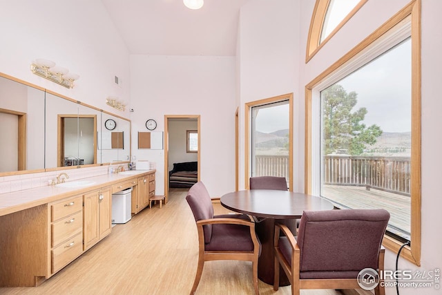 dining area featuring light hardwood / wood-style flooring, high vaulted ceiling, and sink