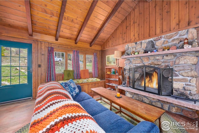 living room with wooden ceiling, hardwood / wood-style flooring, a stone fireplace, vaulted ceiling with beams, and wooden walls