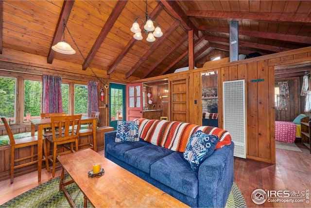 living room featuring a notable chandelier, wooden walls, a wealth of natural light, and lofted ceiling with beams