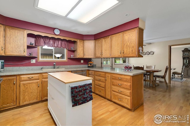 kitchen with light wood-type flooring, kitchen peninsula, a kitchen island, and sink