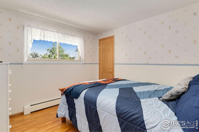 bedroom with a baseboard radiator, hardwood / wood-style floors, and a textured ceiling