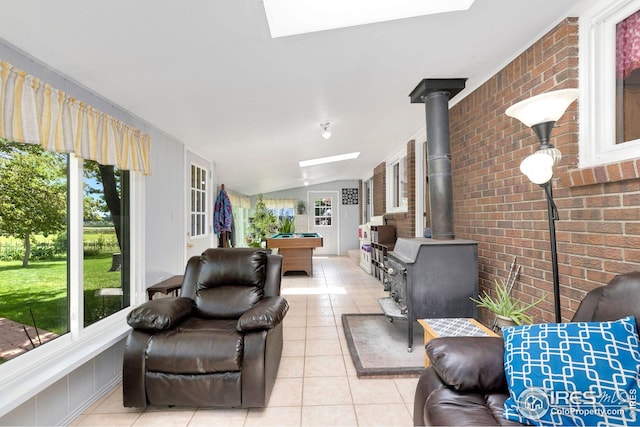 living room featuring light tile patterned flooring, billiards, brick wall, a wood stove, and vaulted ceiling with skylight