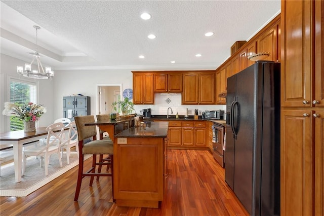 kitchen with a textured ceiling, a notable chandelier, black refrigerator with ice dispenser, brown cabinets, and electric stove
