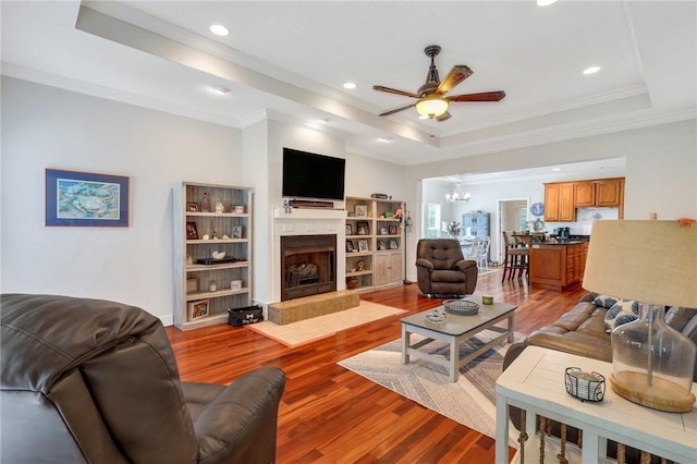 living room featuring a fireplace, a raised ceiling, wood finished floors, and ceiling fan with notable chandelier