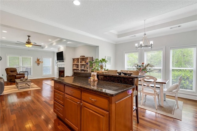 kitchen featuring a center island, brown cabinets, a breakfast bar, a raised ceiling, and dark wood-style floors