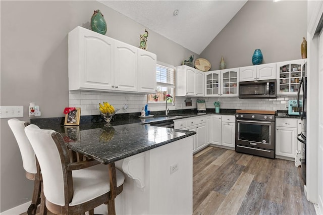 kitchen featuring glass insert cabinets, a peninsula, vaulted ceiling, stainless steel appliances, and a sink