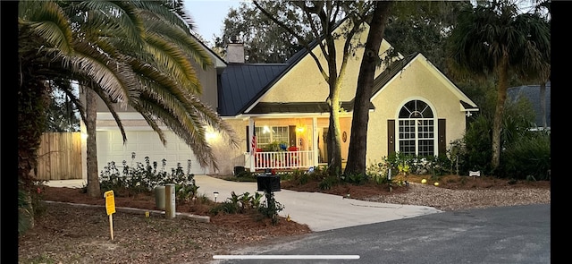 view of front facade with stucco siding, a porch, concrete driveway, an attached garage, and metal roof