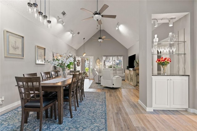 dining space with light wood finished floors, visible vents, track lighting, high vaulted ceiling, and baseboards