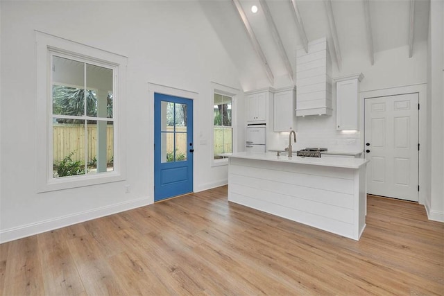 247 Circle Dr, Saint Simons Island, GA 31522 - kitchen featuring light countertops, a kitchen island with sink, white cabinetry, backsplash, and light wood-style flooring