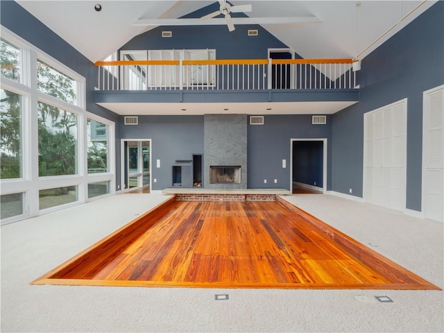 unfurnished living room featuring carpet, ceiling fan, a tile fireplace, and high vaulted ceiling