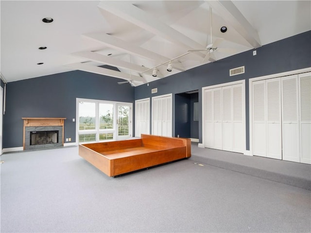 unfurnished bedroom with multiple closets, ceiling fan, a fireplace, and vaulted ceiling with beams