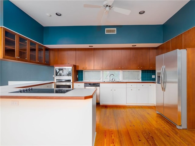 kitchen with light wood-type flooring, stainless steel appliances, ceiling fan, sink, and white cabinets