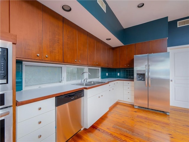 kitchen with backsplash, stainless steel appliances, sink, light hardwood / wood-style flooring, and white cabinets