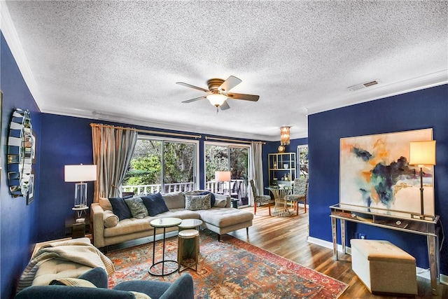 living area with a textured ceiling, wood finished floors, visible vents, baseboards, and a ceiling fan