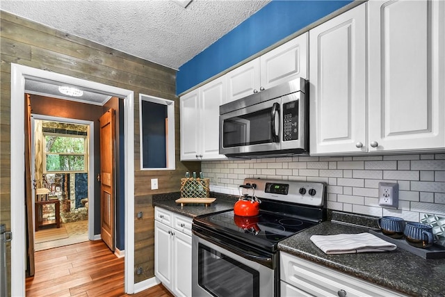 kitchen with white cabinets, wood walls, and stainless steel appliances